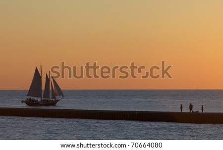 Sunset cruise aboard four sail large ship with the pier and fishermen in the fore ground. Lake Michigan is the setting for this sunset.