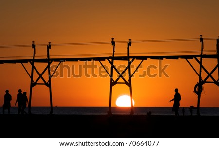 People silhouetted by the sunset as they walk on a pier in Lake Michigan.