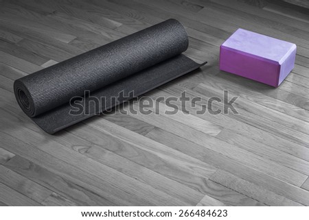 Black and white image of a yoga mat on a wood floor with a pink yoga brick