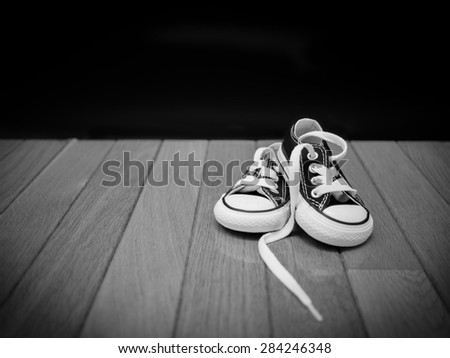 Black and white image of a pair of a small pair of sneakers on a wooden floor with a black background