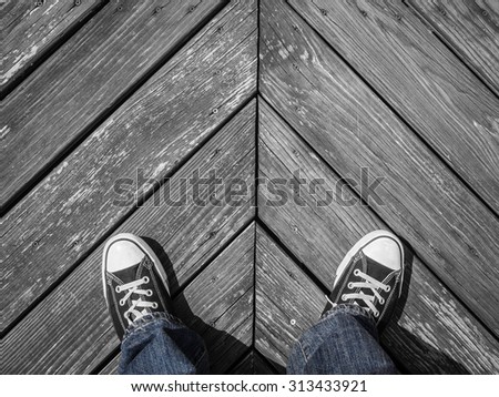 Image of a man\'s legs and feet wearing blue jeans and sneakers on a black and white wooden floor