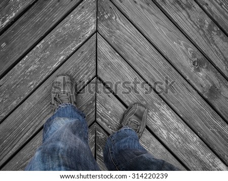 Black and white image with a color splash of a man\'s legs and feet wearing blue jeans and leather shoes standing on a wooden floor