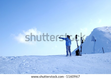 A young woman skier, high on a snowy ridge, pointing out towards the east as the sun sets behind her in the west, and the blue hour begins.