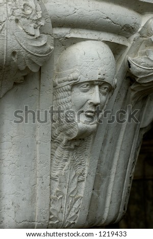 A sculpted soldier\'s head, protected by a helmet and chain mail, at the top of a pillar on the Doge\'s Palace in Venice