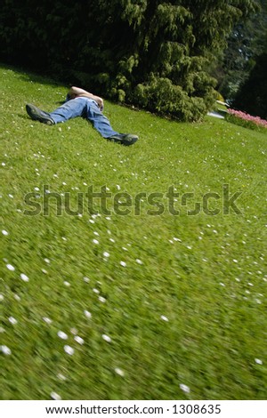 A figure lies, flat out on the grass, as if the earth has suddenly tilted and moved violently. Space for text on the green of the grass in the foreground.