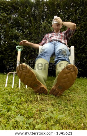 After a hard afternoon digging a gardener slumps back in a seat, exhausted, letting his fork fall to the ground, Space for text on the background to the left, or on the grass of the foreground.