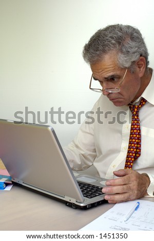 A businessman peers at his laptop computer with intense concentration and a hint of puzzlement. Space for text on the white background.