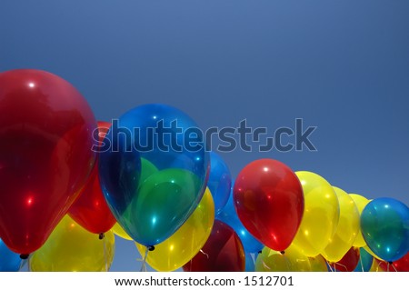 A row of multi-coloured balloons floating against a clear blue sky. A tree can be seen, reflected in the blue one. Space for text in the sky.