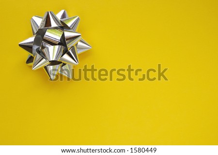 A decorative star, made from silver ribbon, on a plain yellow background with space for text (copy).