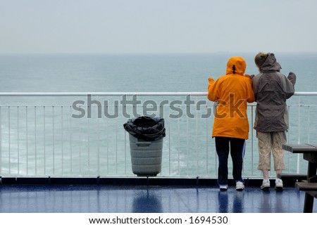 Two young women, in the rain, looking over the rail at a grey sea and waving. A container ship can just be seen on the horizon. Maybe they know someone on the ship.