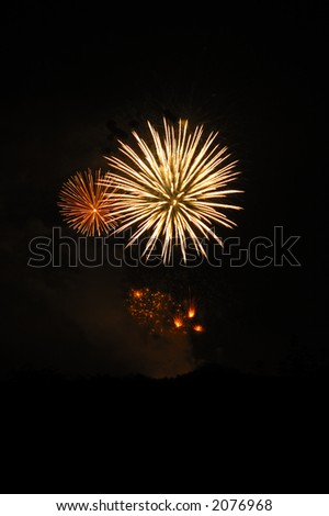 Two firework bursts in the night sky, with others just exploding beneath them. A faint hint of the horizon below. Space for text in the dark of the night sky.