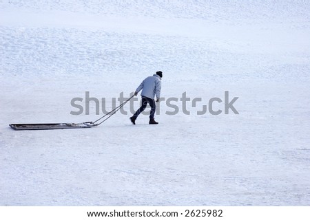 A solitary man drags a sledge across a wide open expanse of snow.