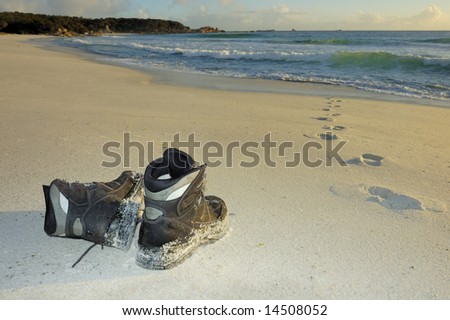 A pair of boots on a sandy beach in the early light of dawn Footprints lead into the sea but do not come out again. Space for copy on the sand.