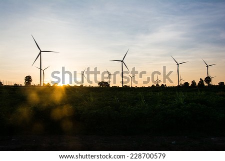 Electric wind turbines farm silhouettes on sun background