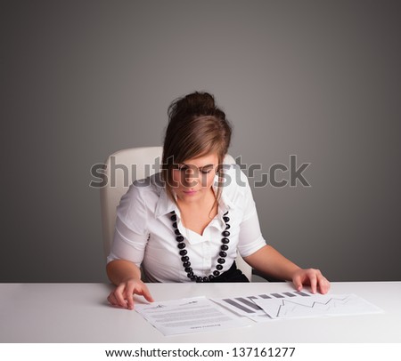 Beautiful young businesswoman sitting at desk and doing paperwork