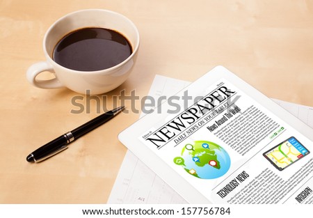 Workplace with tablet pc showing news and a cup of coffee on a wooden work table close-up