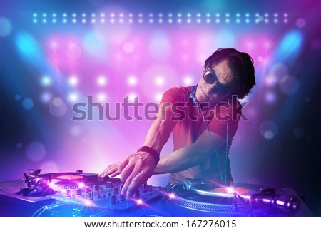 Young disc jockey mixing music on turntables on stage with lights and stroboscopes