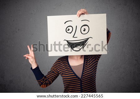 Young woman holding a cardboard with a smiley face on it in front of her head