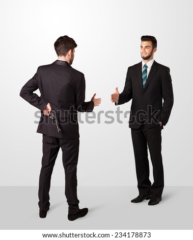 Two opposing businessman shake hands, one of them hiding a weapon behind his back