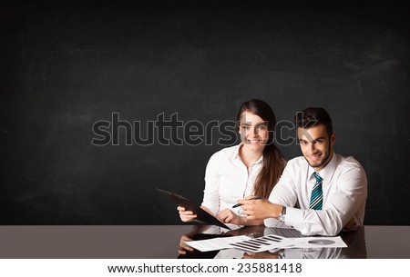 Business couple sitting at black table on black background