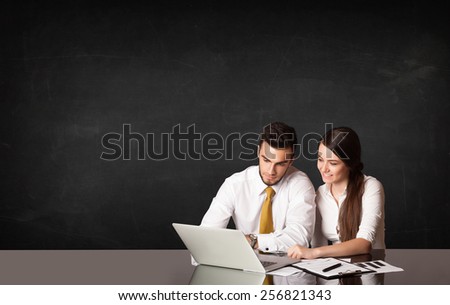 Business couple sitting at black table with a laptop on black background