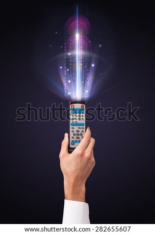 Hand holding a remote control, shining numbers and letters coming out of it