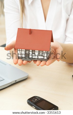 businesswoman holding mini house with a laptop and cell phone