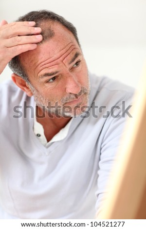 Senior man looking at his hair in mirror