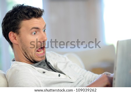 Man in sofa with scared look in front of tablet