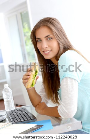 Student girl eating sandwich in front of desktop