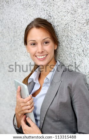 Smiling executive woman leaning on grey wall
