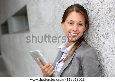 Smiling executive woman leaning on grey wall