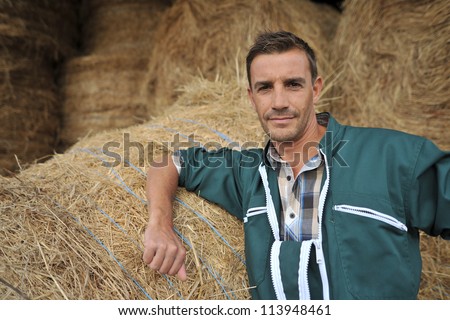Portrait of cheerful farmer standing in front of hay rolls
