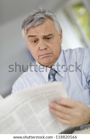 Senior businessman reading news with inquiring look