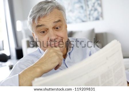 Senior man reading newspaper with puzzled look