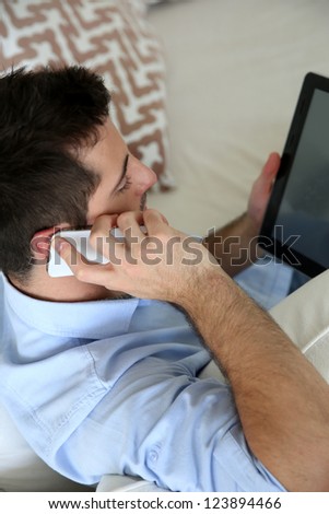 Man sitting in sofa using smartphone and tablet