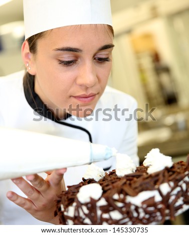 Pastry cook putting whipped cream on cake