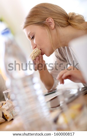 Young woman at work eating sandwich and using tablet