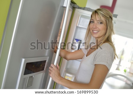 Smiling young woman opening fridge