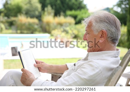 Senior man reading book in pool deck chair