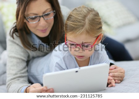 Mother and daughter with eyeglasses playing with tablet