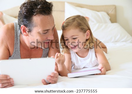 Daddy with daughter on bed playing with digital tablet