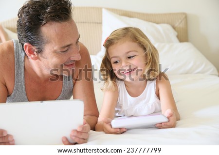 Daddy with daughter on bed playing with digital tablet