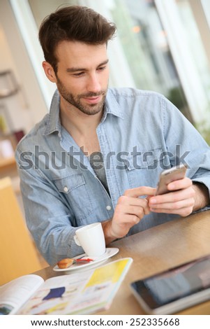 Man in coffee shop sending message with smartphone