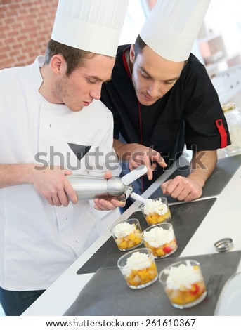 Young cook preparing dessert with chef behind him