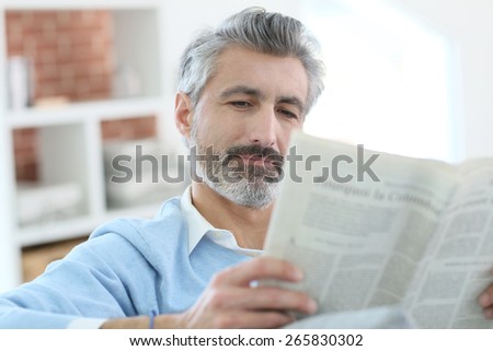 Mature man reading newspaper sitting in sofa