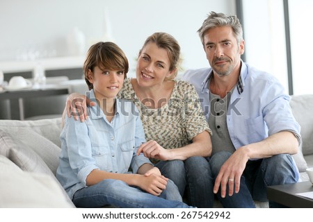 Portrait of happy family of three sitting in sofa at home