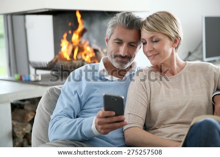 Middle-aged couple using smartphone at home by fireplace
