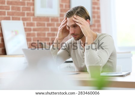Blond guy sitting in front of laptop computer at home