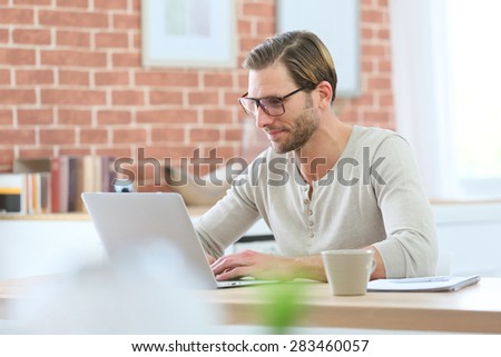 Blond guy with eyeglasses sitting in front of laptop computer at home